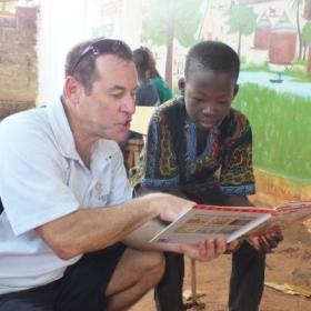 An older volunteer reads to a child as part of his childcare volunteer work overseas